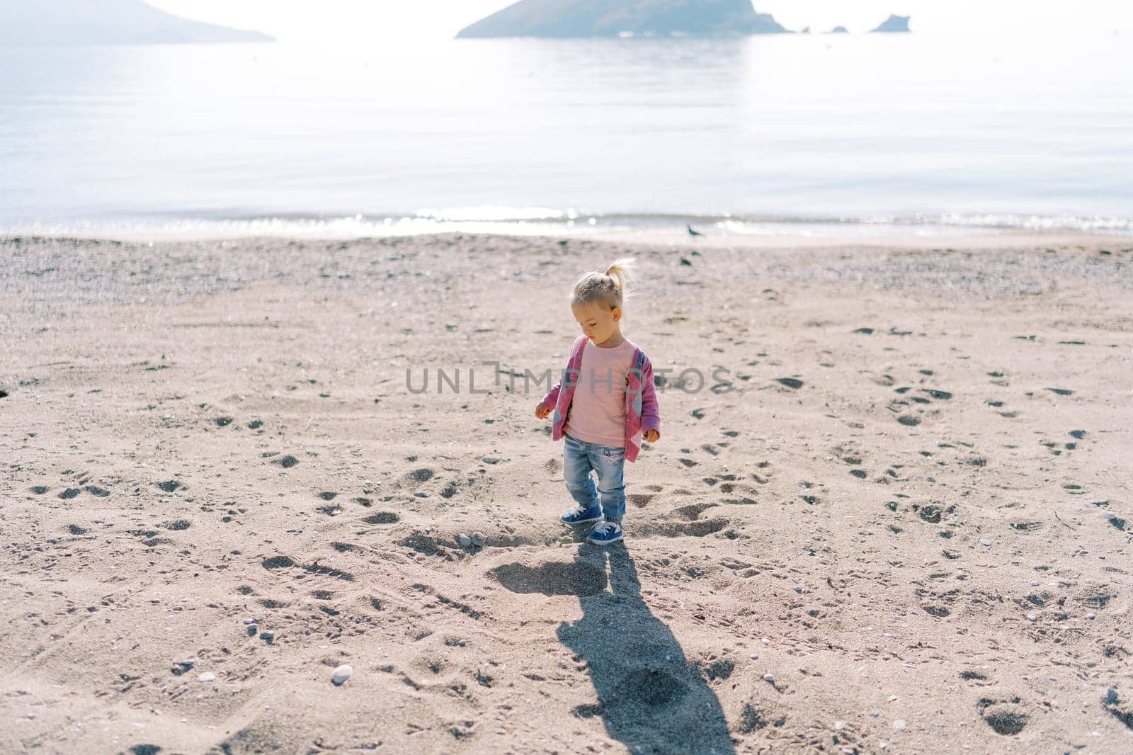Little girl stands on a sandy beach and looks at the hole under her feet. High quality photo