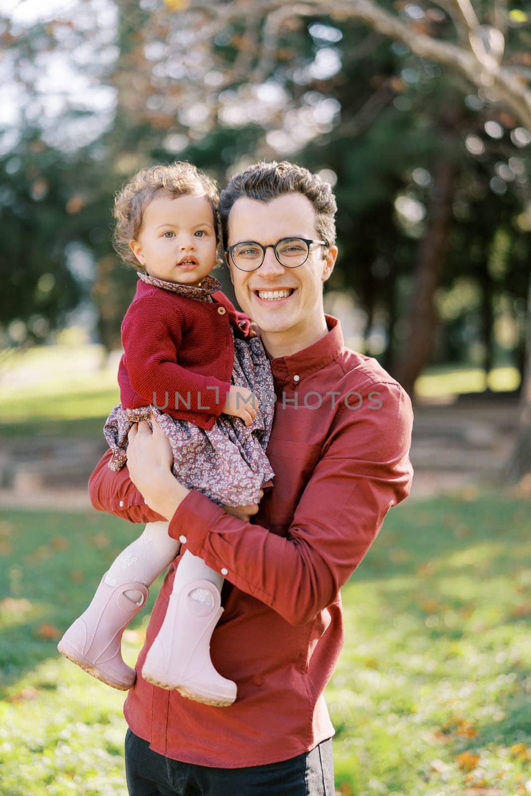 Smiling dad with a little girl in his arms stands in the park. High quality photo