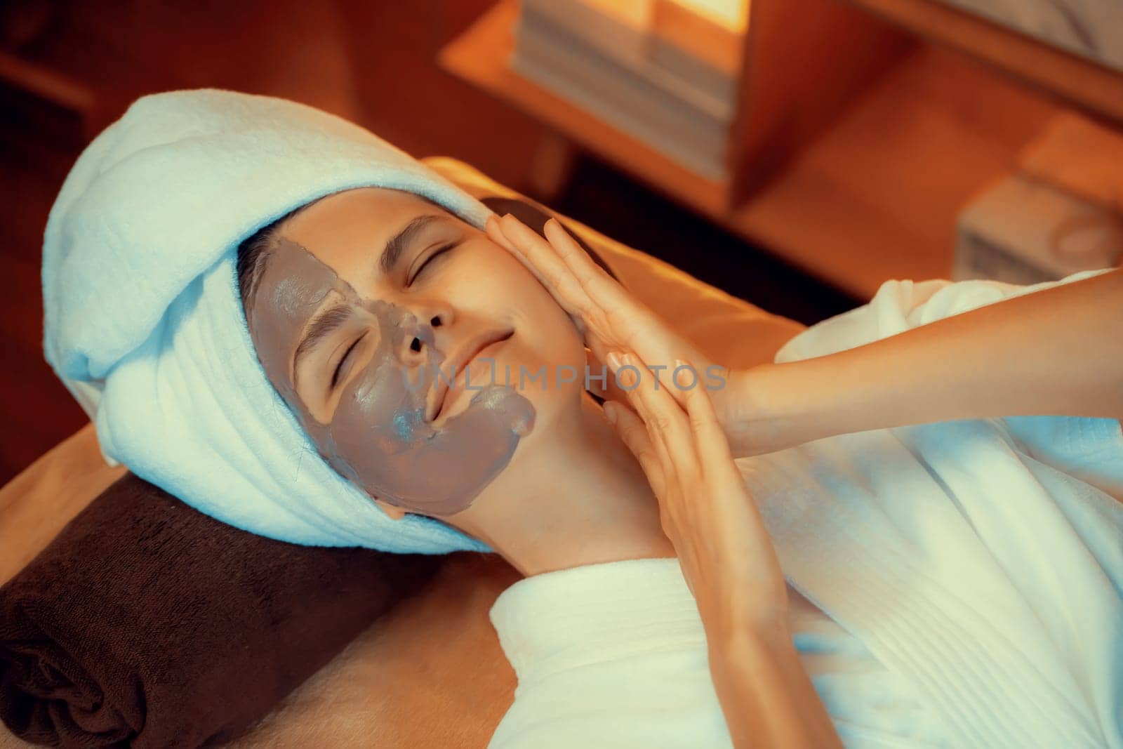 Serene ambiance of spa salon, top view woman customer indulges in rejuvenating with charcoal face cream massage with warm lighting candle. Facial skin treatment and beauty care concept. Quiescent