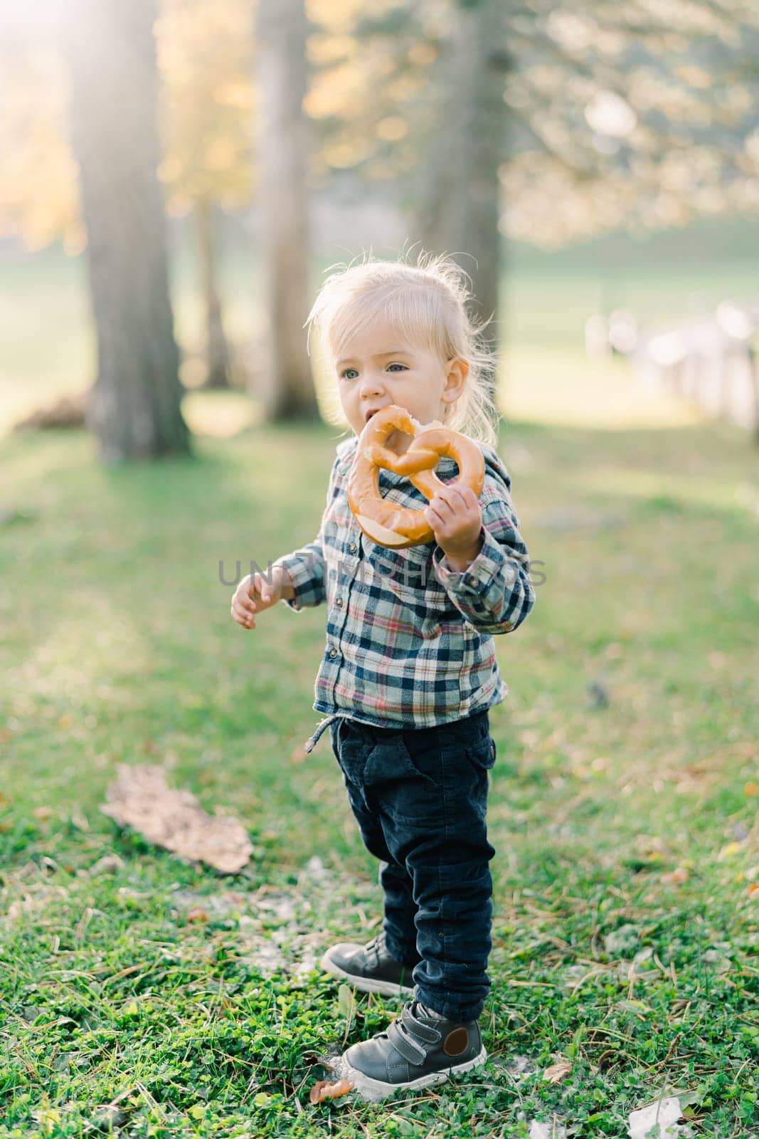 Little girl nibbles a big bagel standing on a green lawn in the park. High quality photo