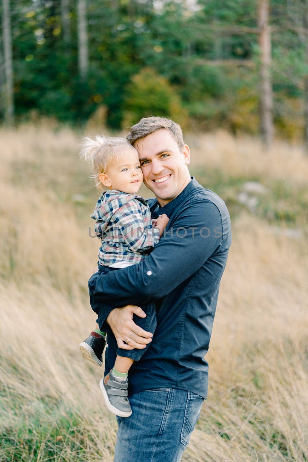 Smiling dad hugging a little girl in his arms while standing in a clearing. High quality photo
