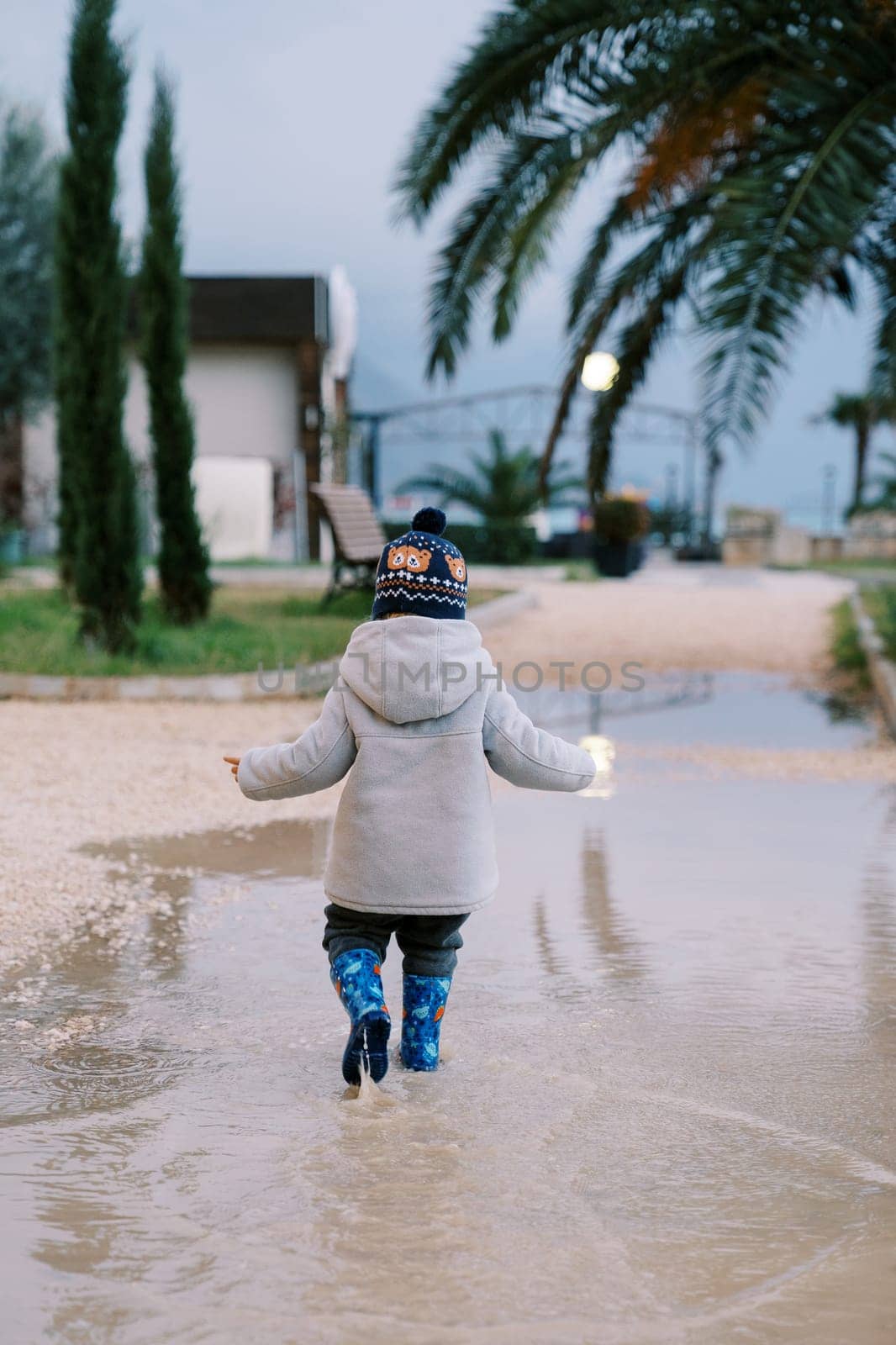Little girl walks through a puddle looking down at her feet. Back view. High quality photo