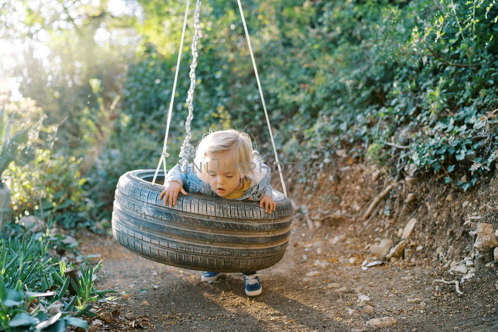 Little girl swings on a tire swing, leaning on her belly by Nadtochiy