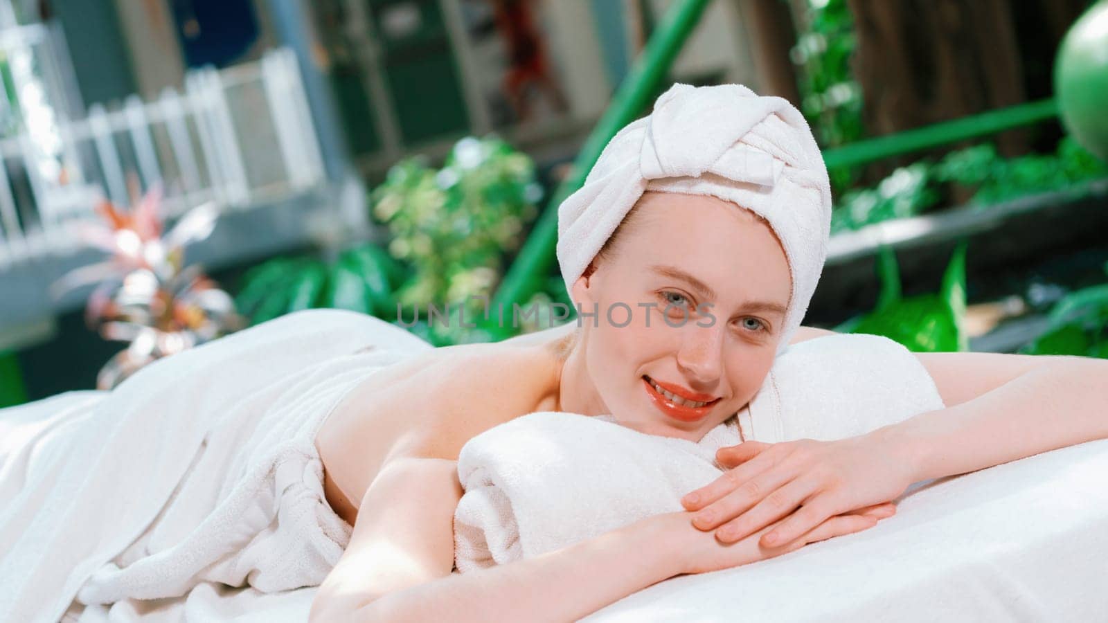 Beautiful young woman relaxes on a spa bed surrounded by nature. ready for a body massage. Attractive female in white towel lying peacefully during waiting for body massage. Close up. Tranquility