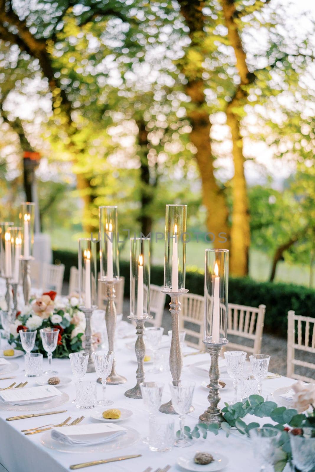 Festive table with lit candles and bouquets of flowers in the garden by Nadtochiy