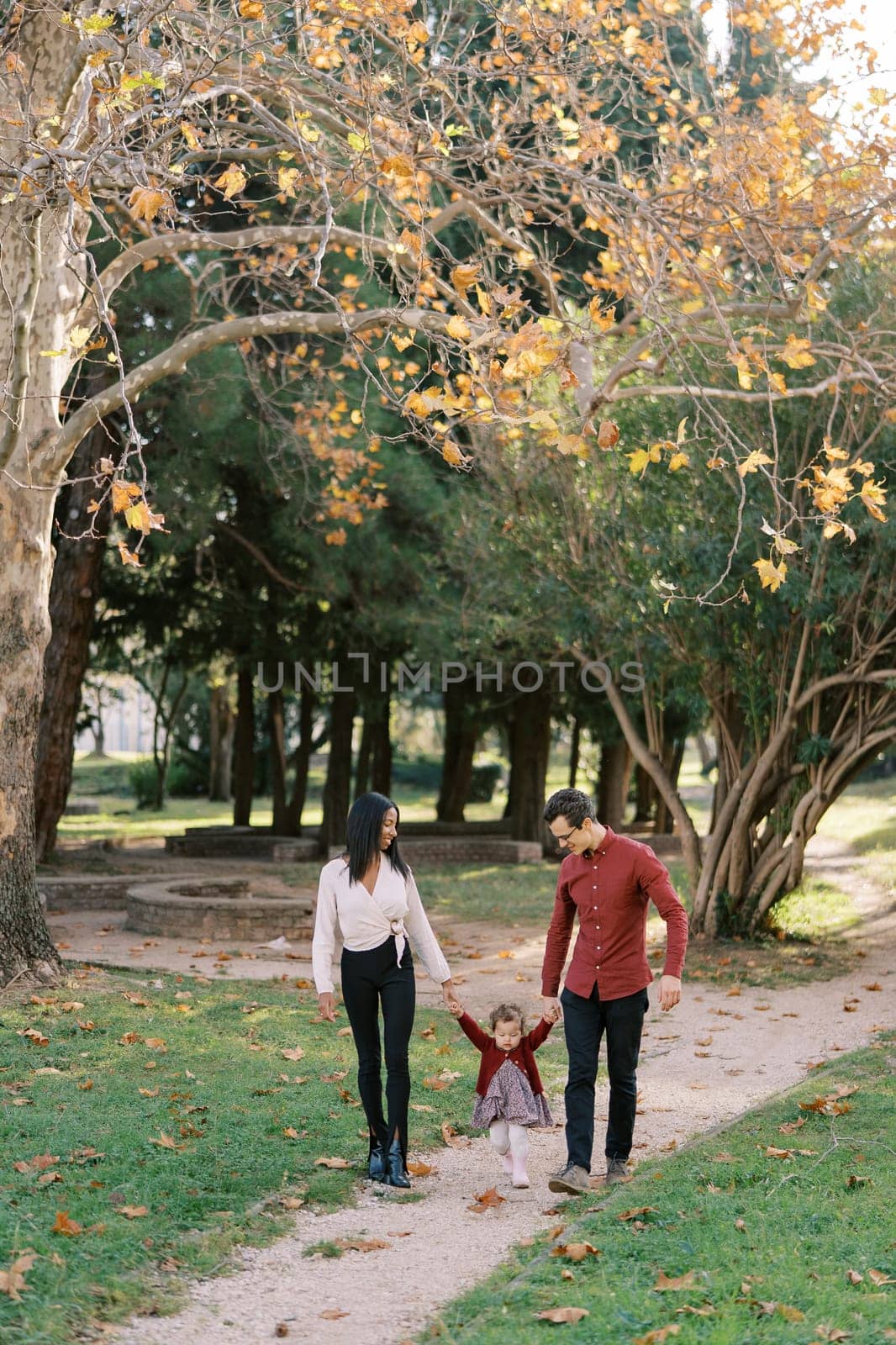 Mom and dad with a little girl walk along the path in the park, holding hands. High quality photo