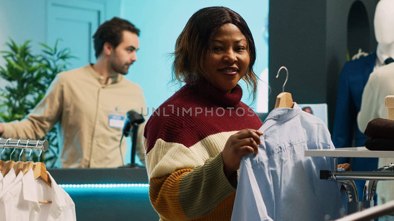 Female client looking at clothes on hangers and racks, examining merchandise in clothing store. Young woman buying fashionable casual wear on discount, commercial activity in shopping center.