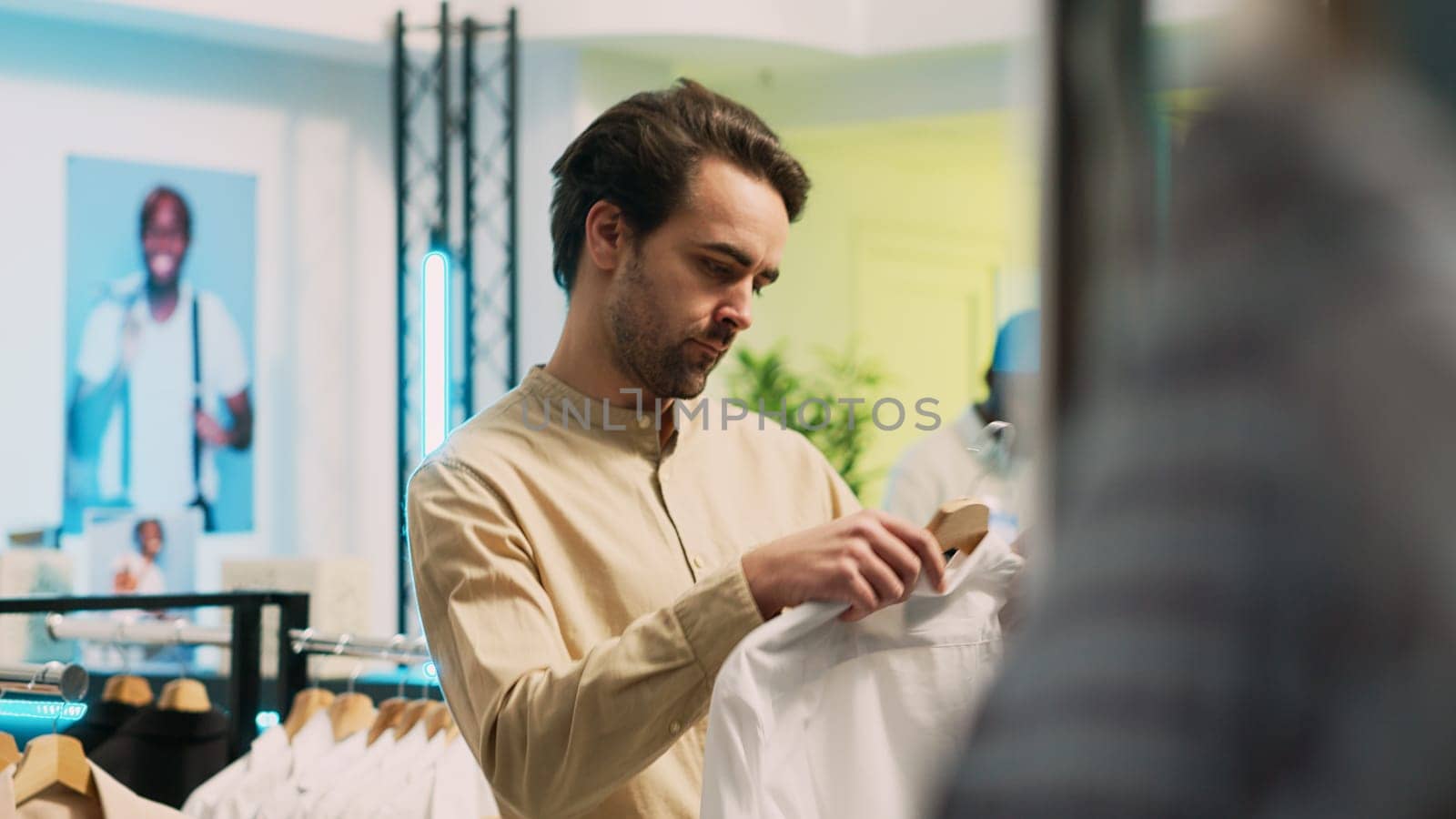 Caucasian man looking at fashionable wear on hangers, buying modern clothes on sale in shopping center. Male customer examining fashion boutique merchandise, commercial activity. Handheld shot.