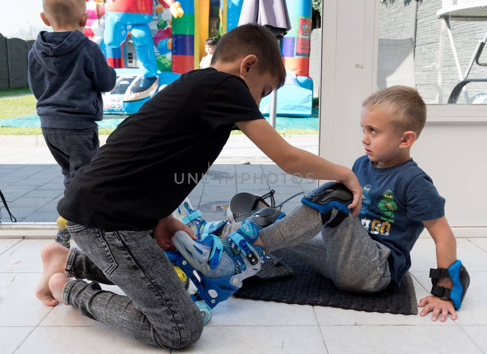 best friend helping his friend put on roller skates as a birthday gift, fun day with friends,a group of children doing sports independently, High quality photo