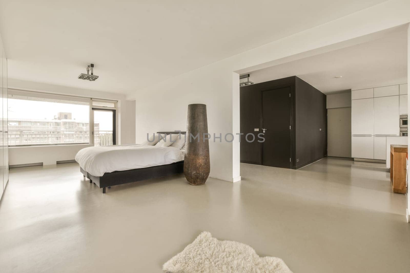 a modern bedroom with white walls and flooring, there is a large bed in the room has an area rug on the floor