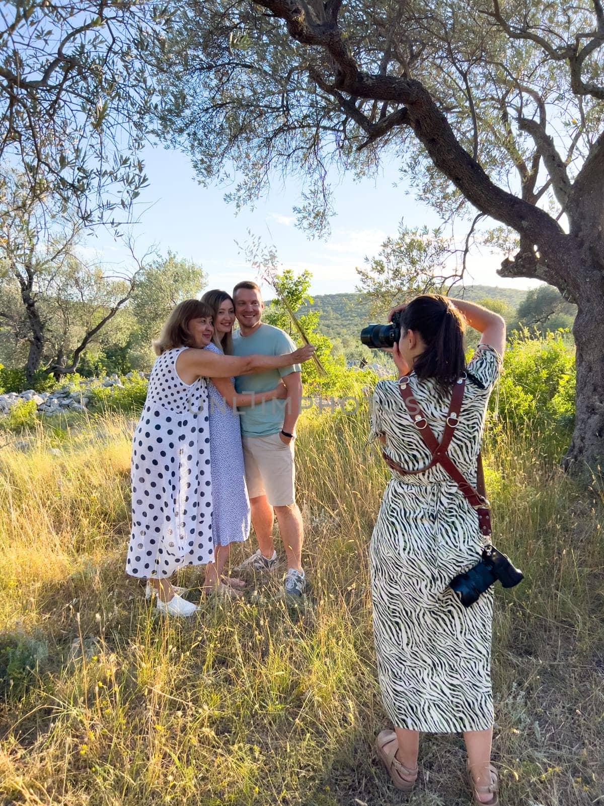 Girl photographer takes pictures of an elderly woman hugging a couple. High quality photo
