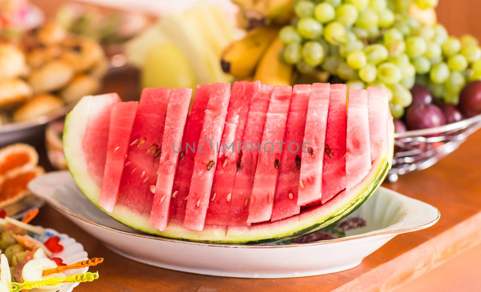 Sliced watermelon on a dish. Sweet berry on the table. The pink flesh of watermelon for dessert. Healthy food for vegetarians. Festive table setting with fruit and berries.