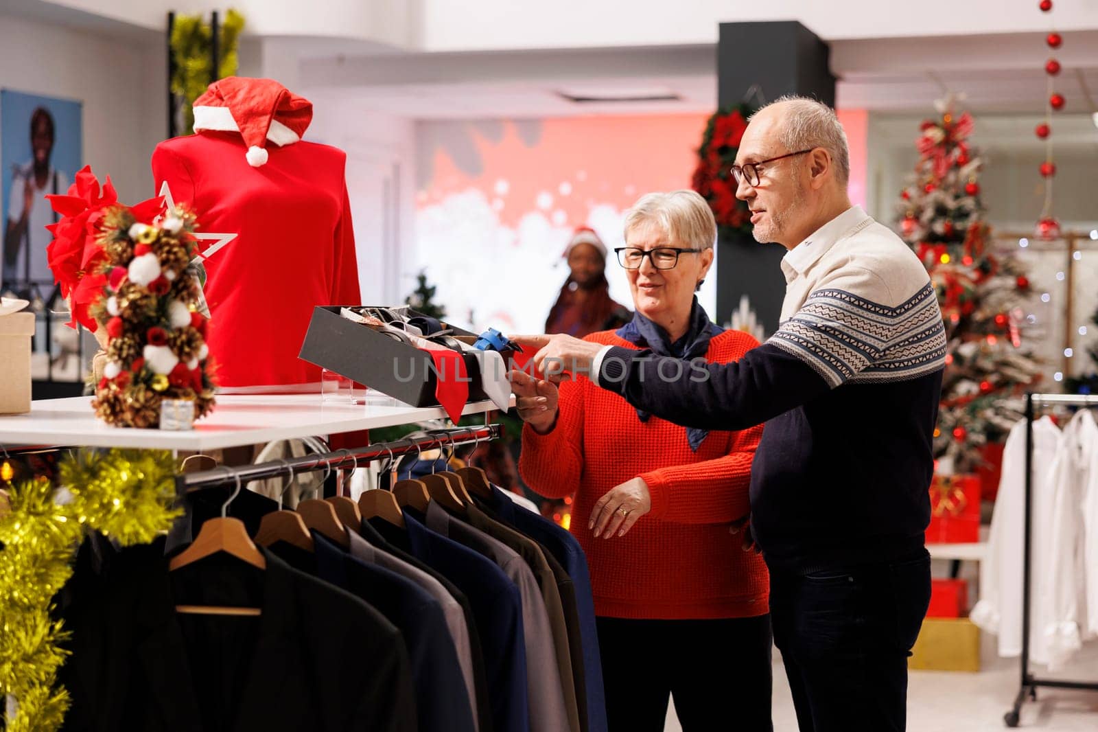 Old customers checking belts and ties in clothing store, looking at accessories to match formal attire for christmas eve dinner outfit. Senior couple searching for clothes during winter sales.