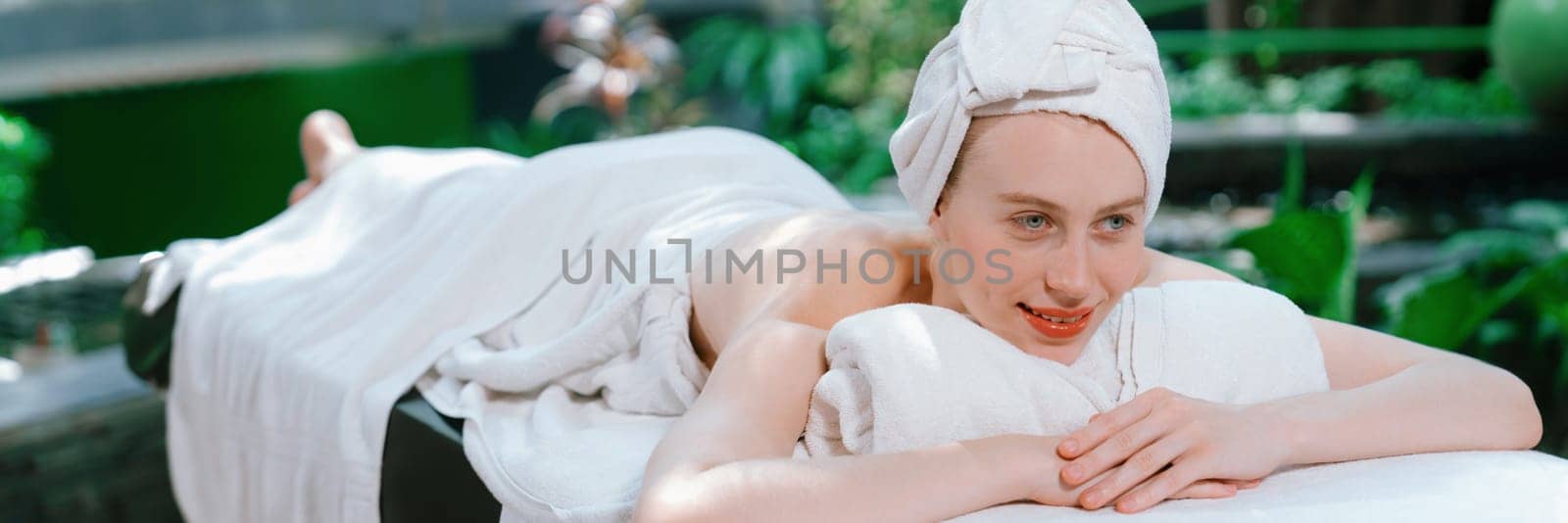 Beautiful young woman relaxes on a spa bed surrounded by nature. ready for a body massage. Attractive female in white towel lying peacefully during waiting for body massage. Close up. Tranquility