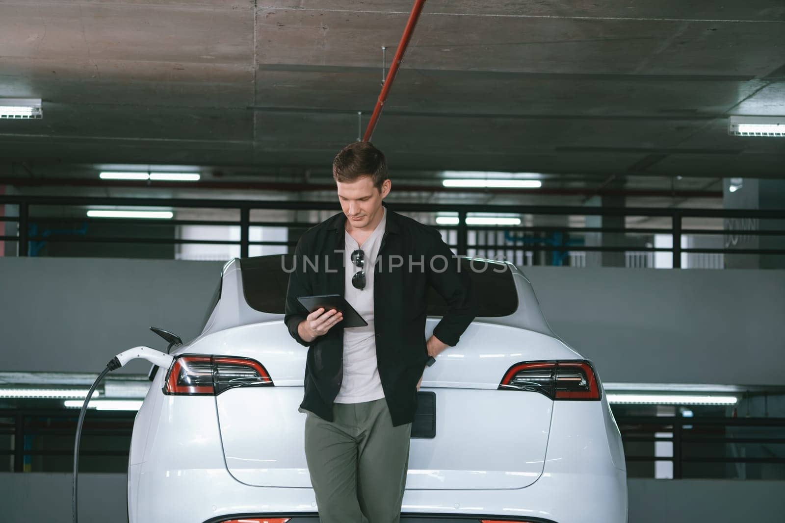 Young man travel with EV electric car to shopping center parking lot charging in downtown city showing urban sustainability lifestyle by green clean rechargeable energy of electric vehicle innards