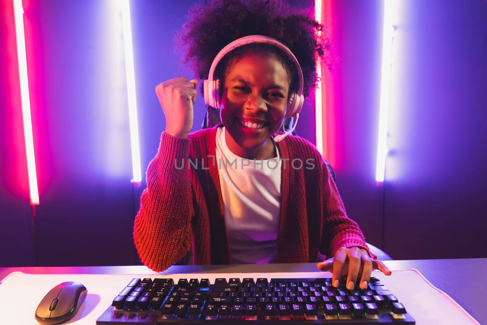 Gaming streamer, African girl playing online fighting with Esport skilled team wearing headphones in neon color lighting room. Talking other players planing strategies to win competitors. Tastemaker.