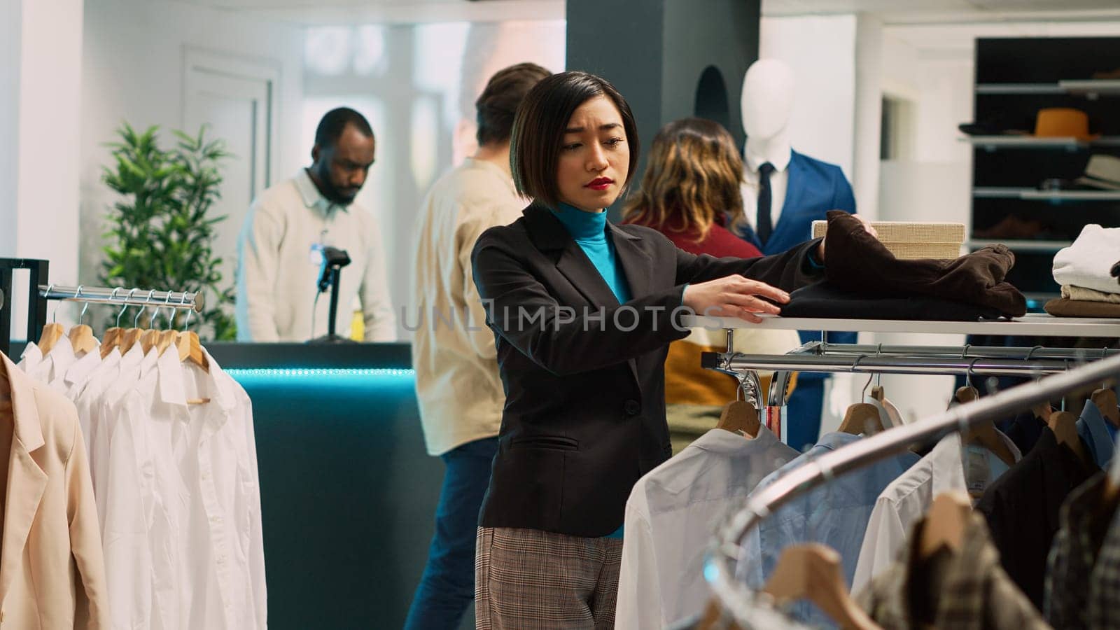 Asian woman shopping in fashionable clothing store, looking at formal and casual wear on hangers. Female customer buying trendy merchandise from shopping center, retail shop. Tripod shot.