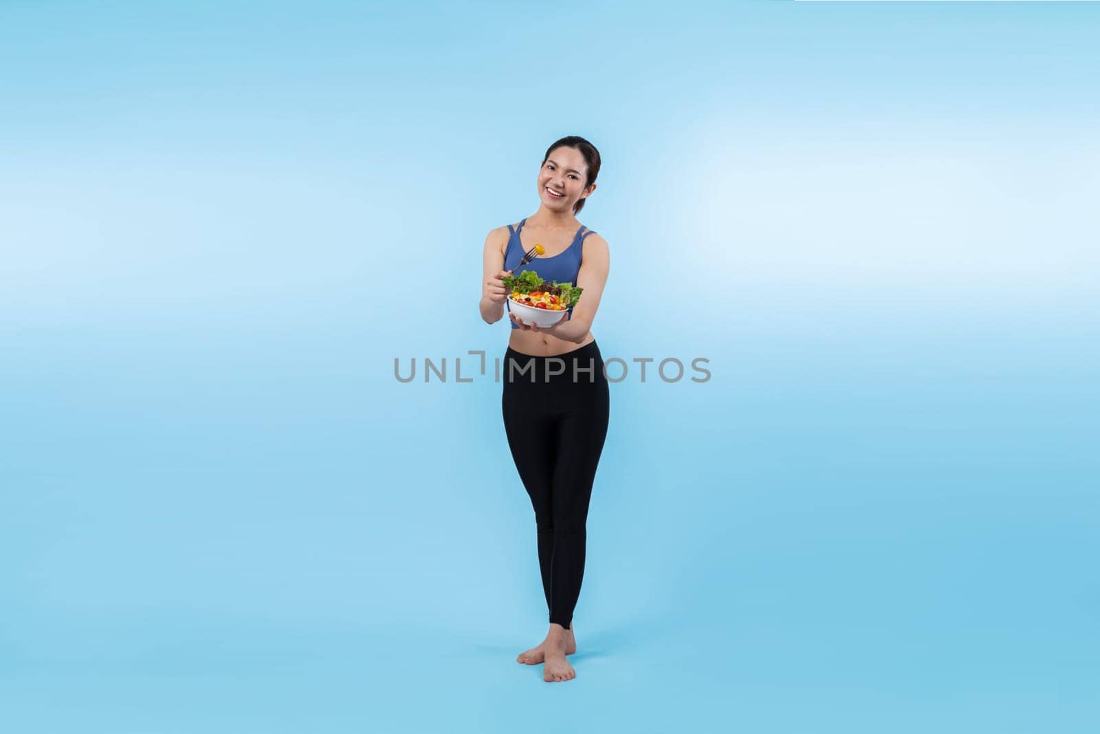 Asian woman in sportswear holding salad bowl on isolated background. Vigorous by biancoblue