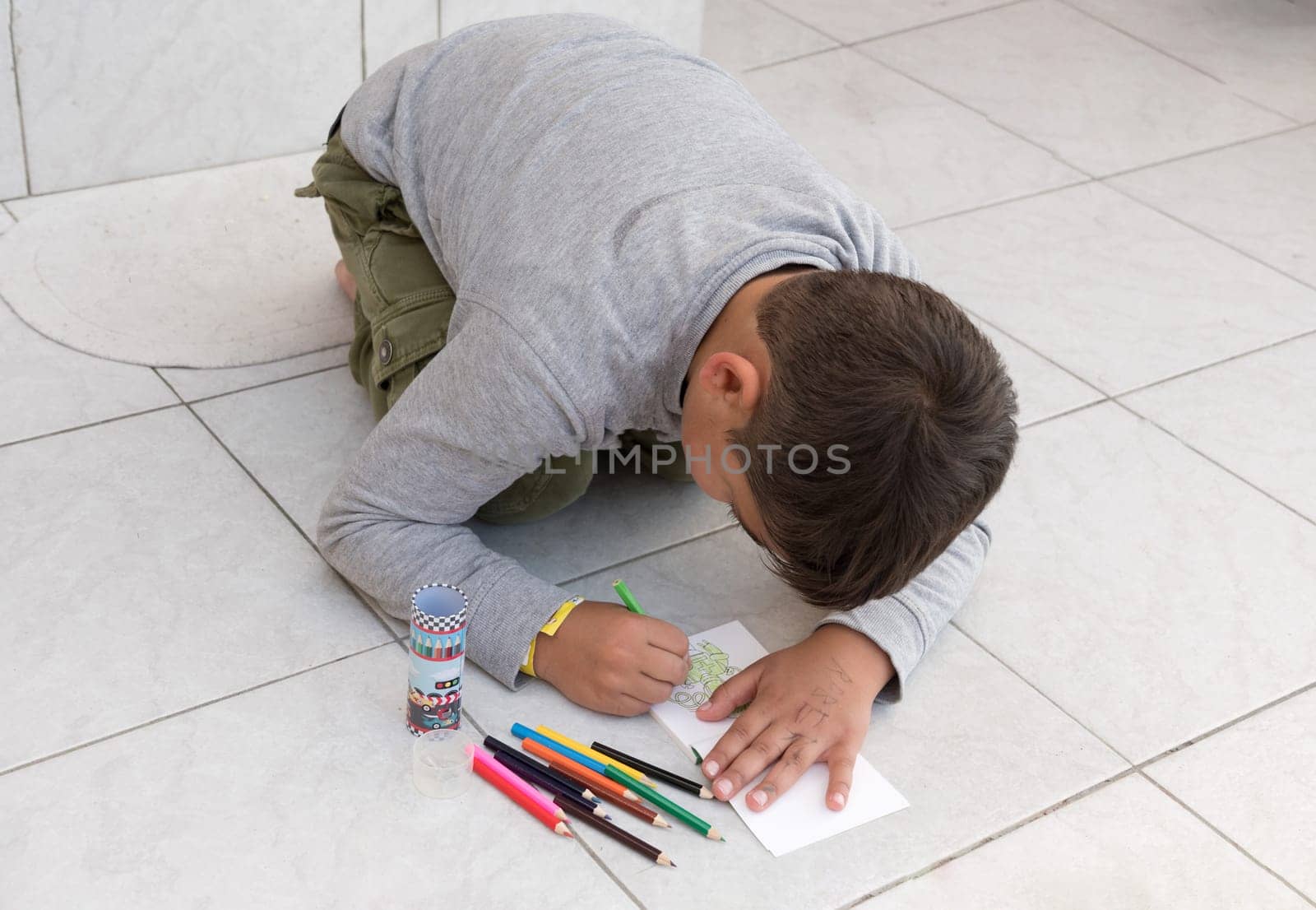 A black-haired boy draws on the floor in his notebook with colored pencils, there are no limits to creativity by KaterinaDalemans