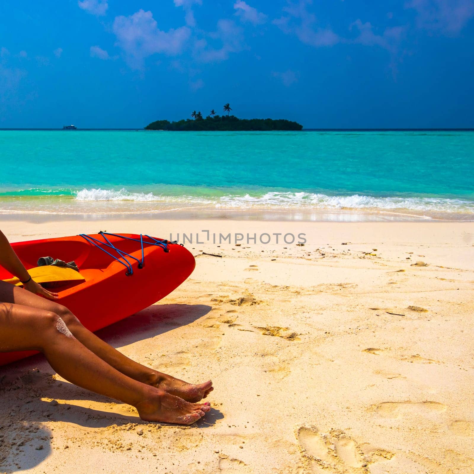 Canoe boat on the white sand of the turquoise sea and sexy womens feet on Rasdhoo island in Rasdhoo Atoll Maldives.