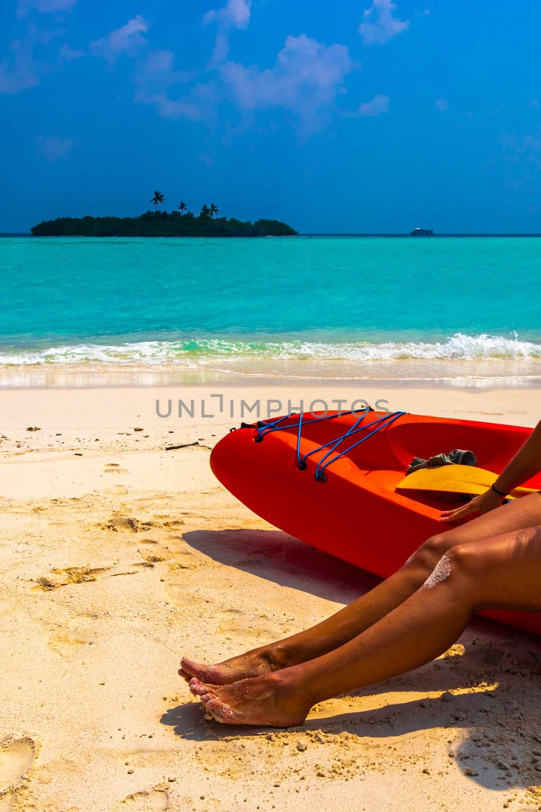 Canoe boat on the white sand of the turquoise sea and sexy womens feet on Rasdhoo island in Rasdhoo Atoll Maldives.