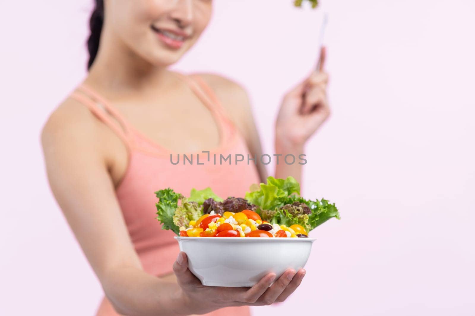 Young sporty Asian woman in sportswear holding salad bowl fill with vibrant of fruit and vegetable. Natural youthful and fit body lifestyle with balance nutrition on isolated background. Vigorous