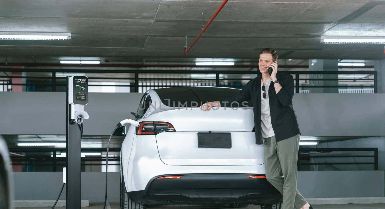 Young man travel with EV electric car to shopping center parking lot charging in downtown city showing urban sustainability lifestyle by green clean rechargeable energy of electric vehicle innards