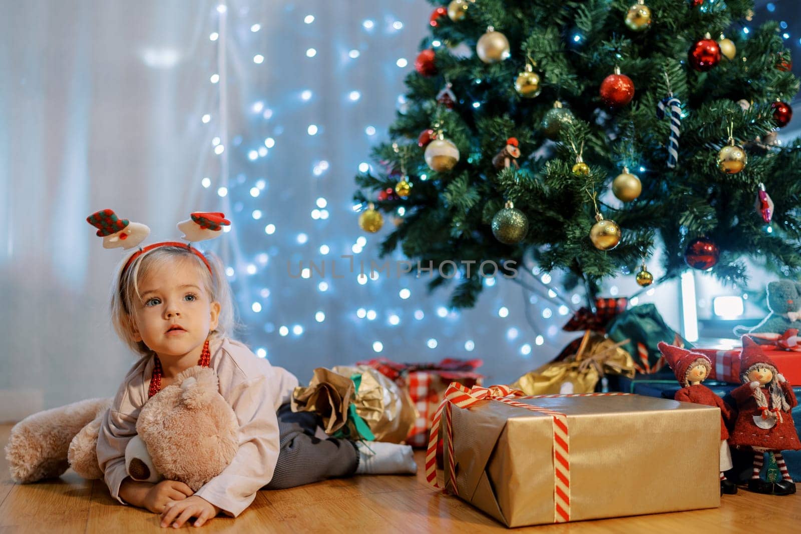 Little girl hugging a teddy bear while sitting near the gifts near the Christmas tree. High quality photo