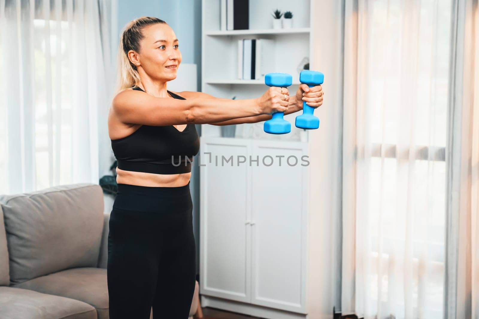 Athletic and sporty senior woman engaging in body workout routine with lifting dumbbell at home as concept of healthy fit body with body weight lifestyle after retirement. Clout