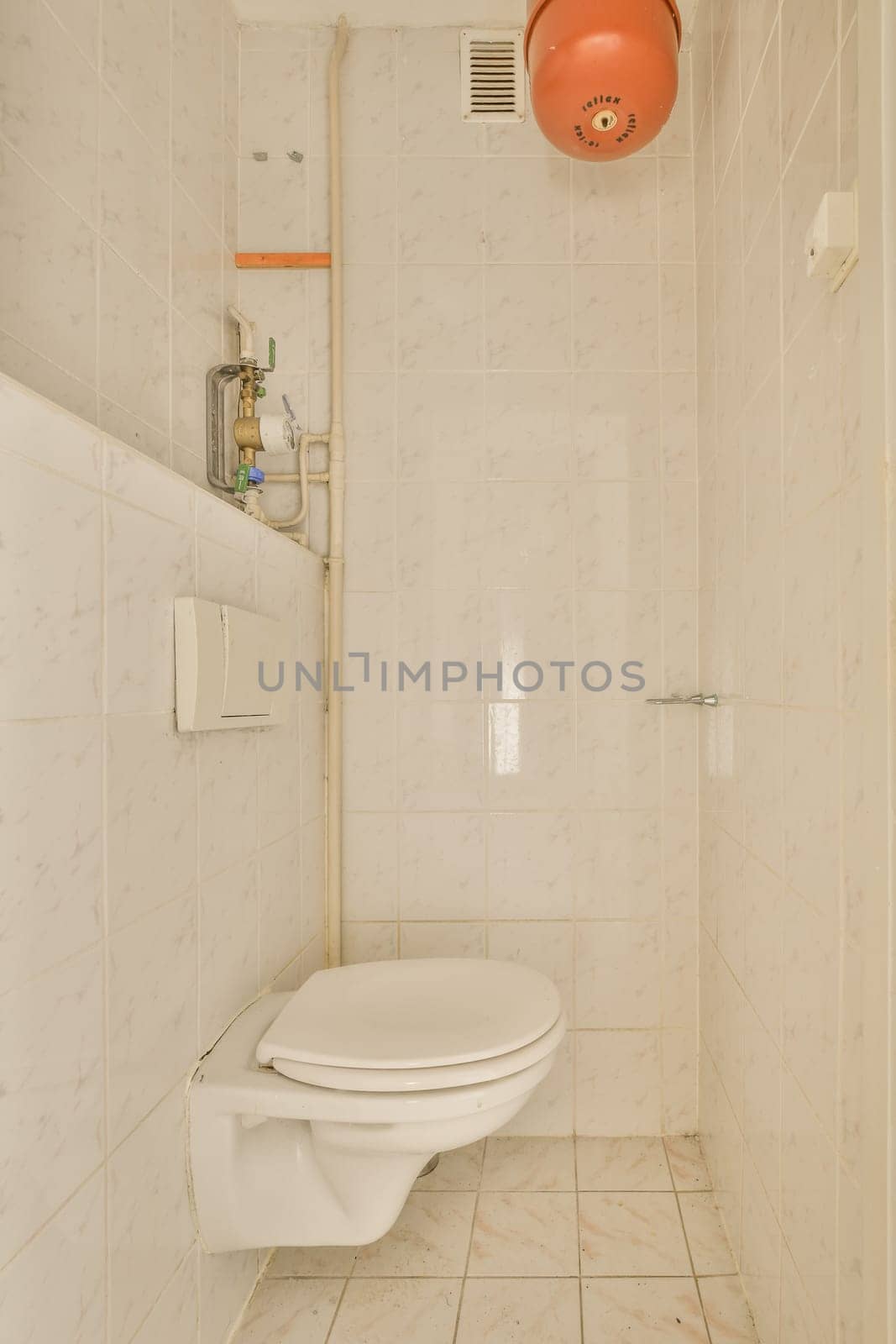 a bathroom with a toilet and an orange ball hanging on the wall in front of the toilet is white marble tiles