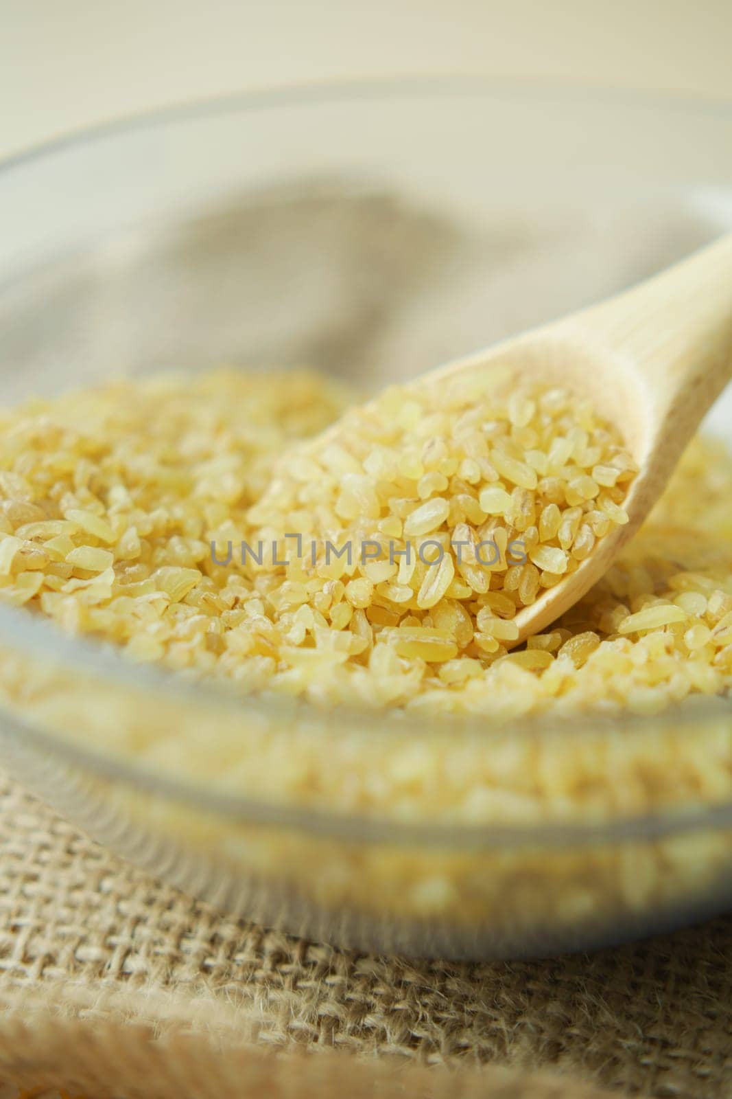 raw bulgur with wooden spoon in a bowl on table by towfiq007