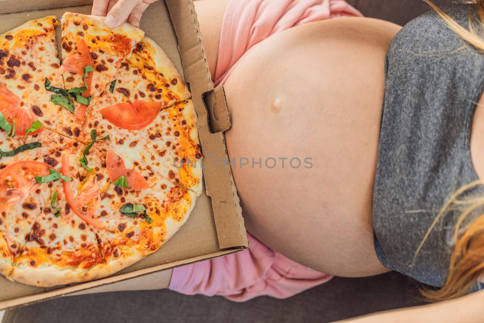 A pregnant woman enjoys a slice of pizza, savoring a moment of indulgence while satisfying her craving for a delightful, comforting treat. Excited Pregnant Young Lady Enjoying Pizza Holding Biting Tasty Slice Posing With Carton Box. Junk Food Lover Eating Italian Pizza. Unhealthy Nutrition Cheat Meal by galitskaya