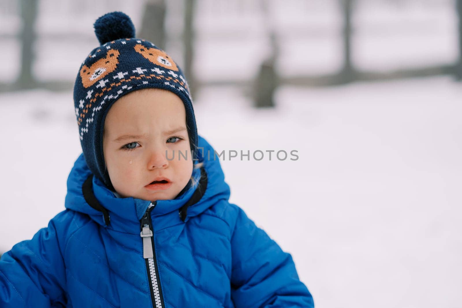 Little sad girl with tearful eyes stands on the snow in the forest. High quality photo