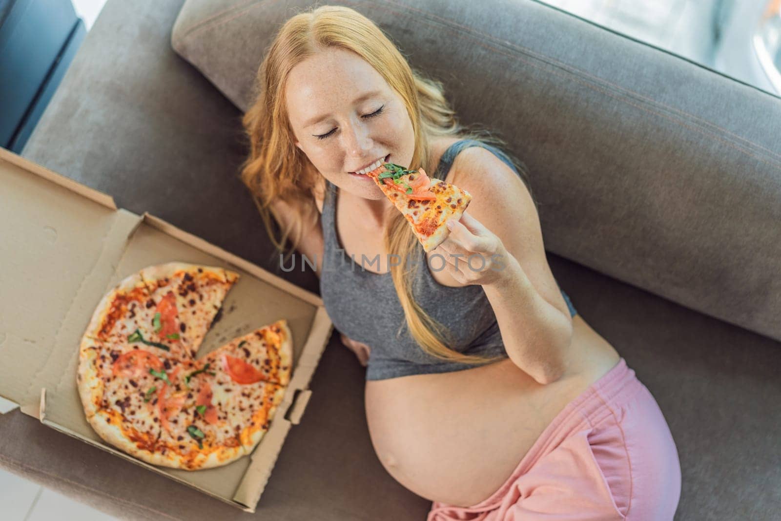 A pregnant woman enjoys a slice of pizza, savoring a moment of indulgence while satisfying her craving for a delightful, comforting treat. Excited Pregnant Young Lady Enjoying Pizza Holding Biting Tasty Slice Posing With Carton Box. Junk Food Lover Eating Italian Pizza. Unhealthy Nutrition Cheat Meal by galitskaya