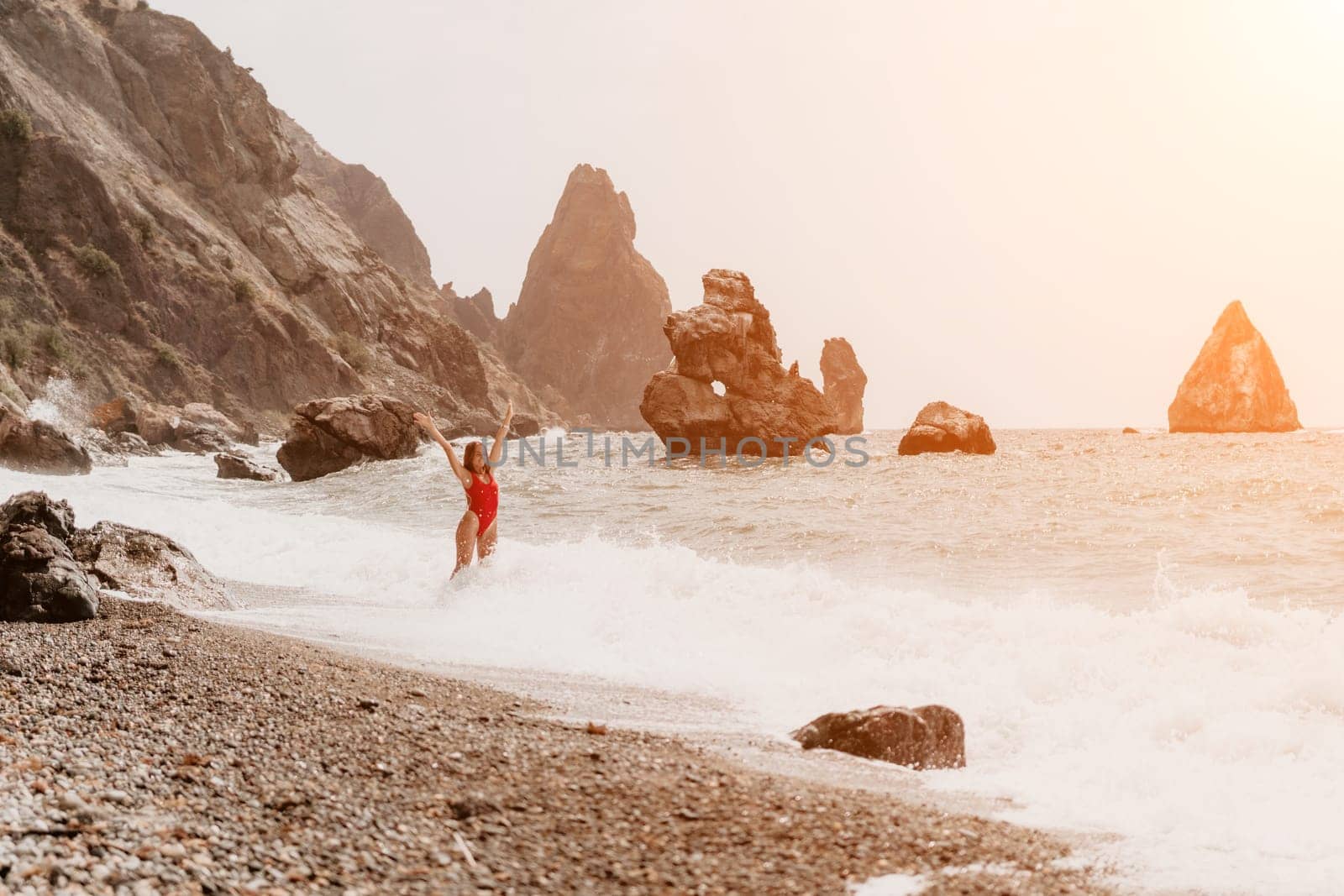 Woman travel sea. Young Happy woman in a long red dress posing on a beach near the sea on background of volcanic rocks, like in Iceland, sharing travel adventure journey