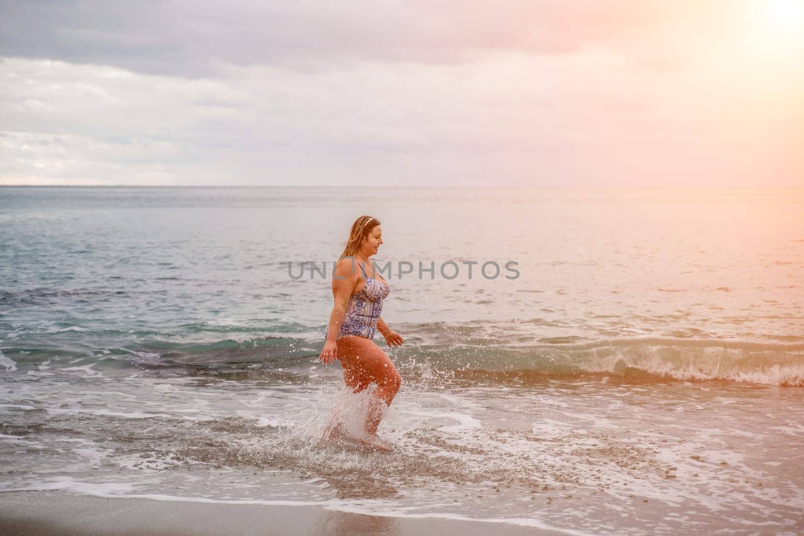 A plump woman in a bathing suit enters the water during the surf. Alone on the beach, Gray sky in the clouds, swimming in winter