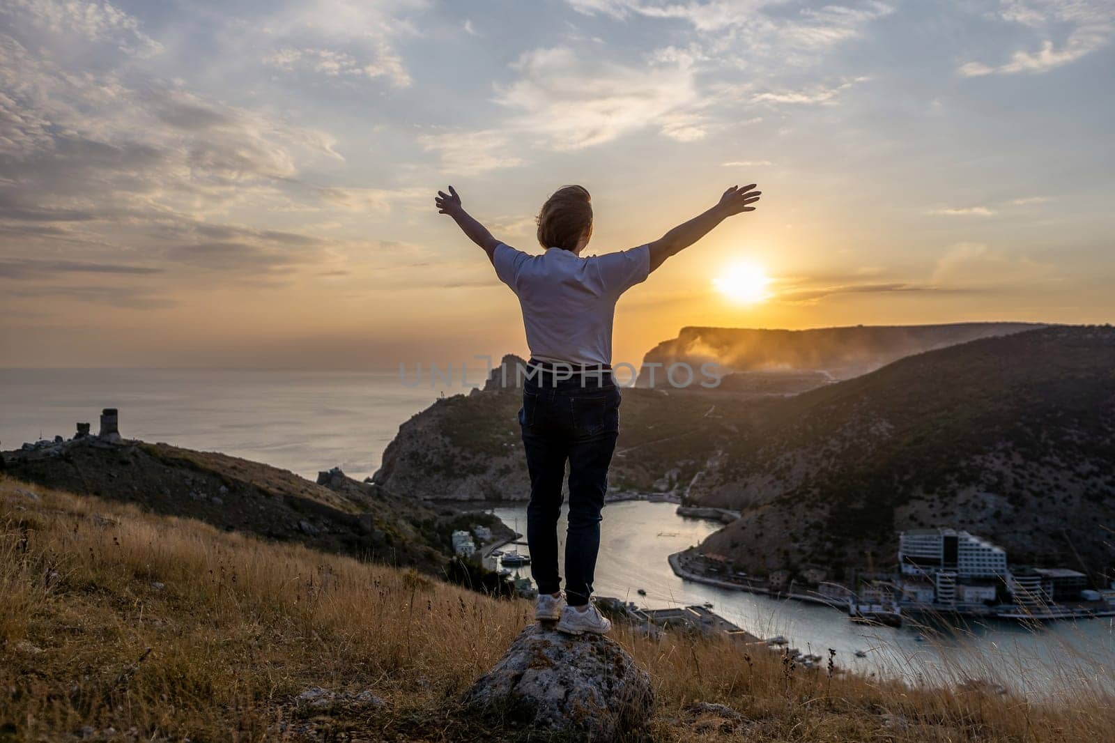 Happy woman on sunset in mountains. Woman standing with her back on the sunset in nature in summer with open hands. Silhouette