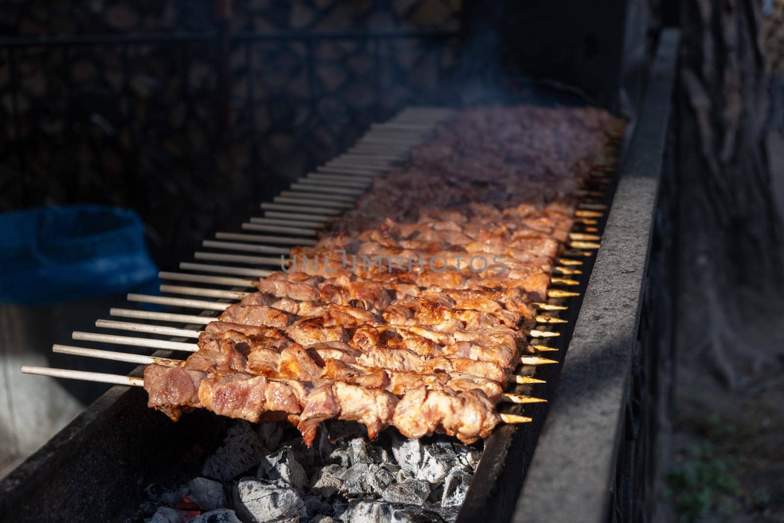 A lot of juicy meat kebabs in a row on the grill. Meat pieces strung on wooden skewers on the grill. The process of cooking kebabs with a lot of smoke. Cooking in nature