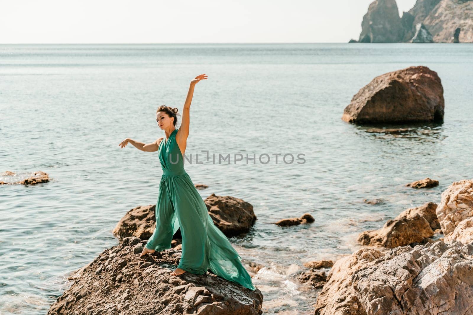 Woman green dress sea. Woman in a long mint dress posing on a beach with rocks on sunny day. Girl on the nature on blue sky background. by Matiunina