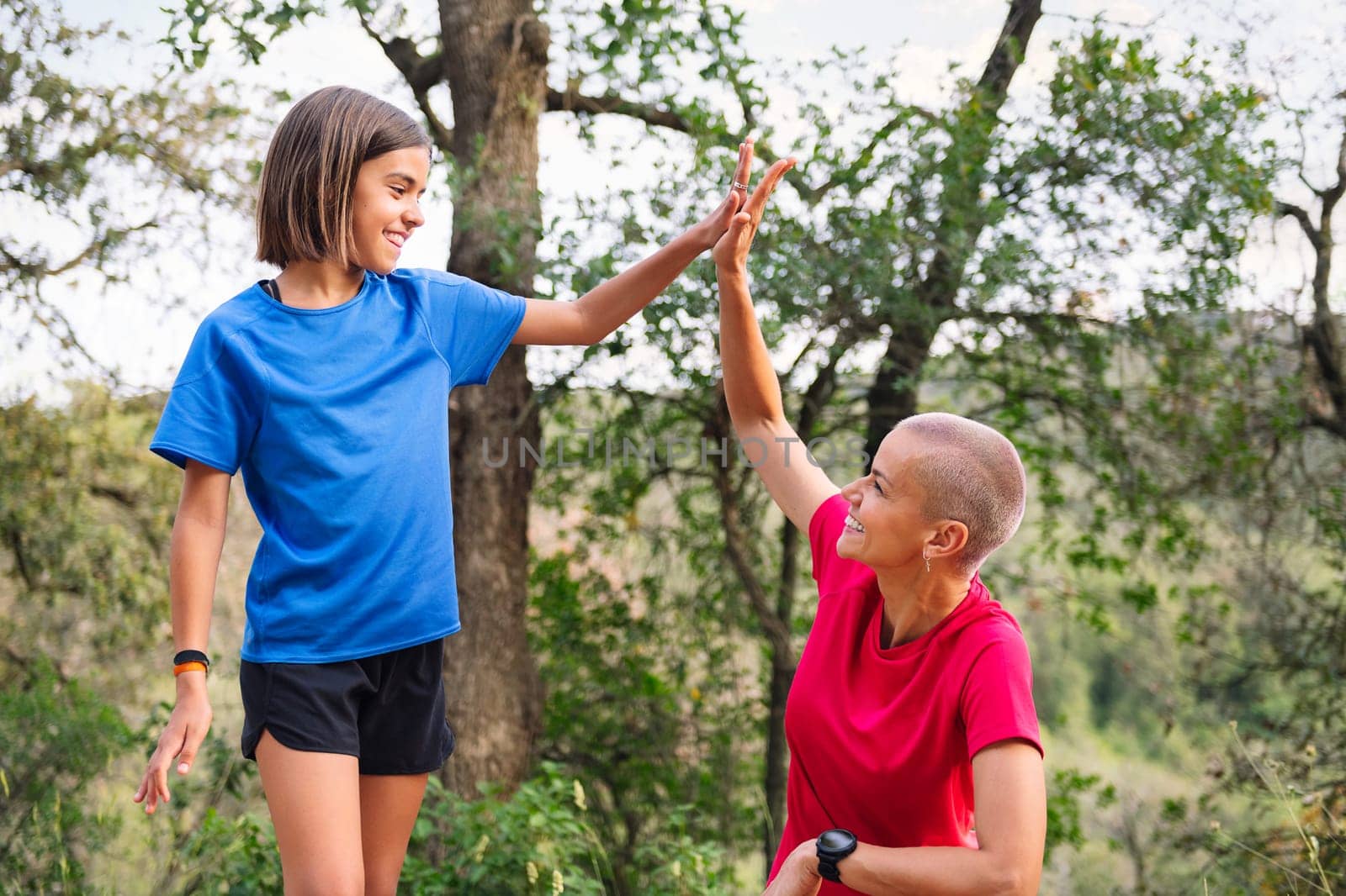 mother and daughter giving a high five during their training in the woods, concept of sport with children in nature and active lifestyle