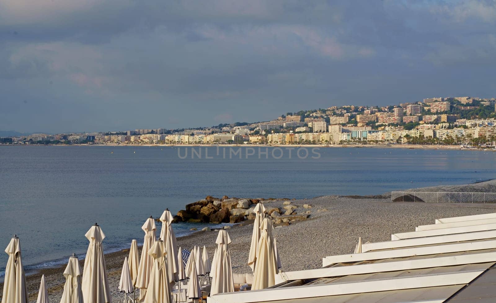 Early morning atmosphere and folded white umbrellas in Nice, France. White umbrellas on the beach against a blue clear sky. Panorama of the beach in Nice by aprilphoto