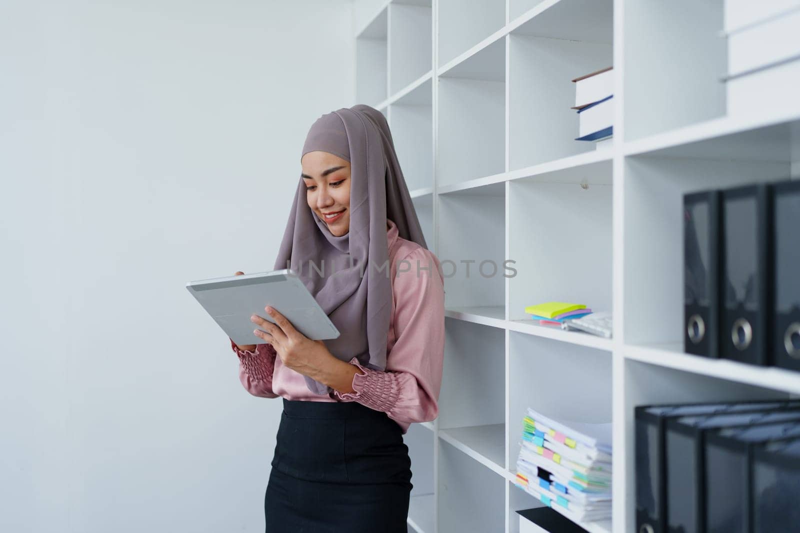 Female Muslim employee uses tablet to work at office. by Manastrong