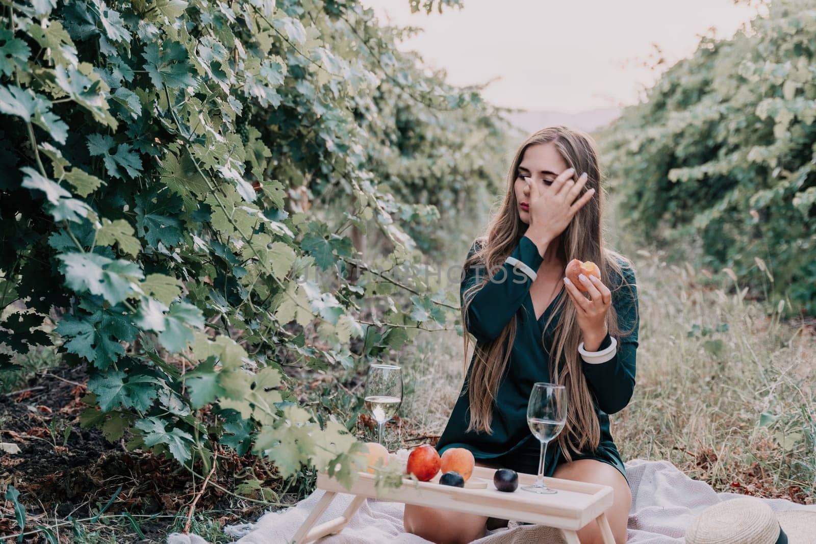 Woman picnic vineyard. Happy woman with a glass of wine at a picnic in the vineyard, wine tasting at sunset and open nature in the summer. Romantic dinner, fruit and wine. by panophotograph