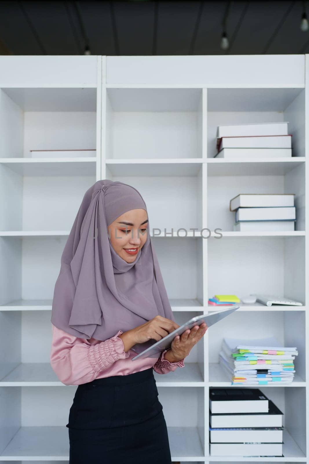 Female Muslim employee uses tablet to work at office. by Manastrong