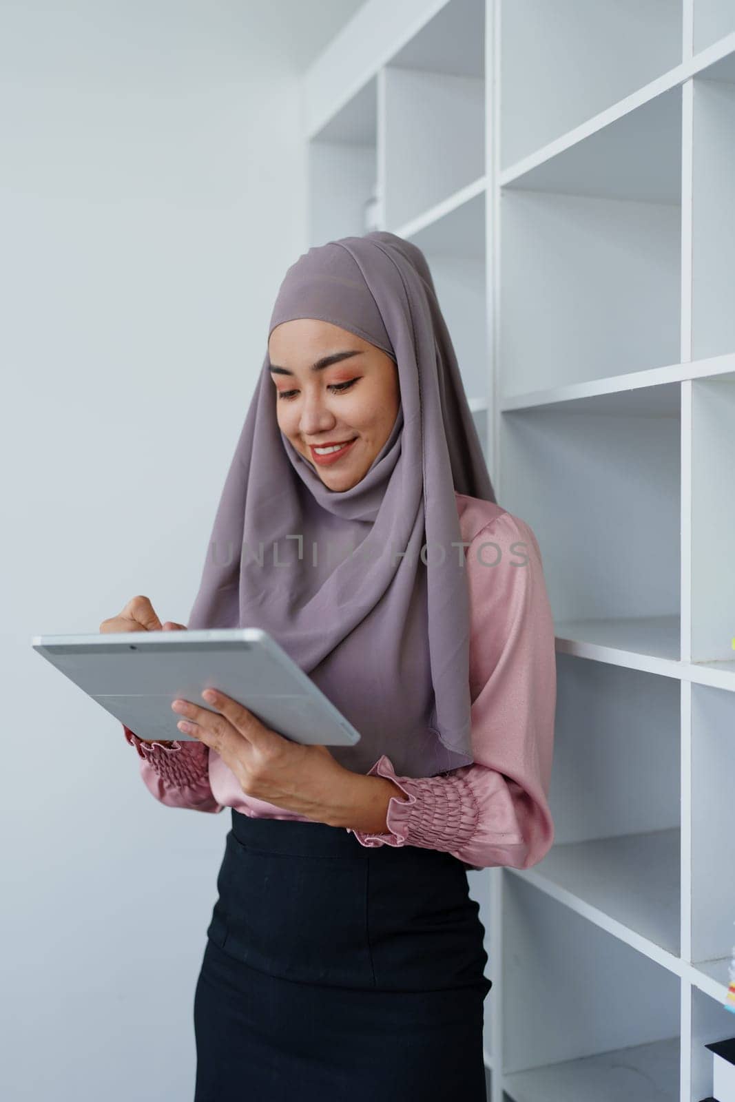 Female Muslim employee uses tablet to work at office. by Manastrong