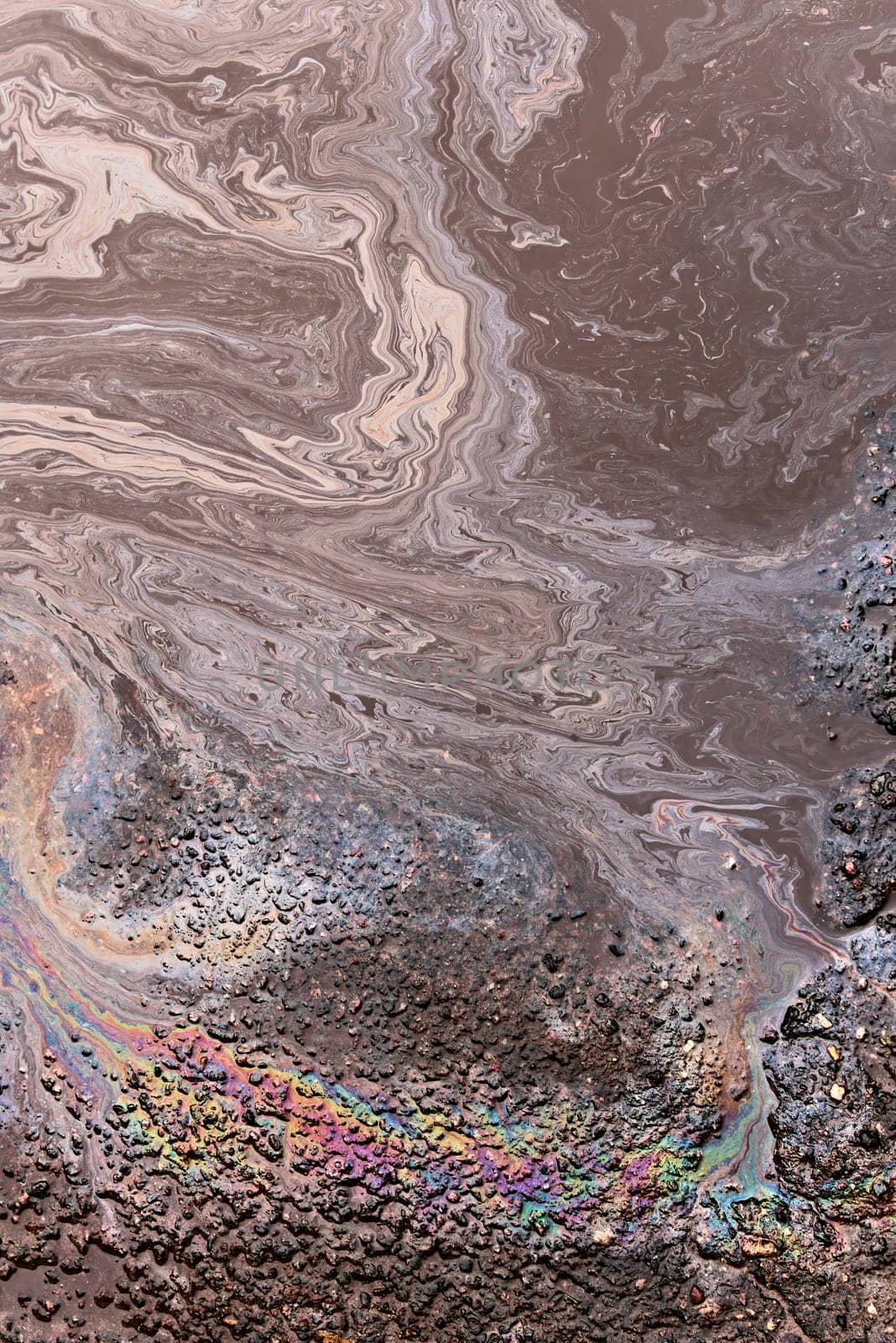 Rainbow-colored oil floating on water after rain on asphalt. Gasoline stains. Colored texture, natural background.