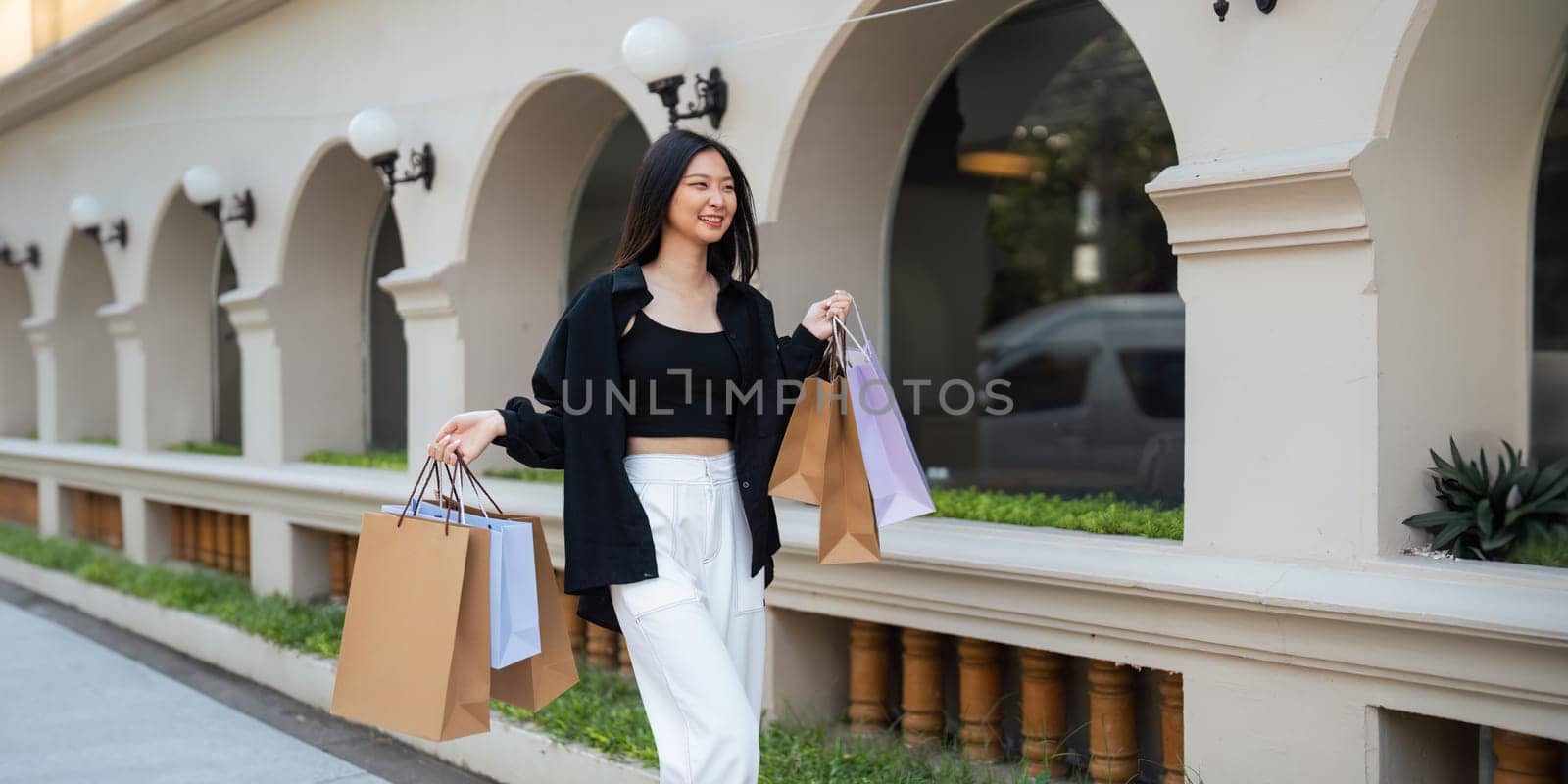 Happy beautiful young stylish woman asian with shopping bag while walking near mall on holiday Black Friday by nateemee