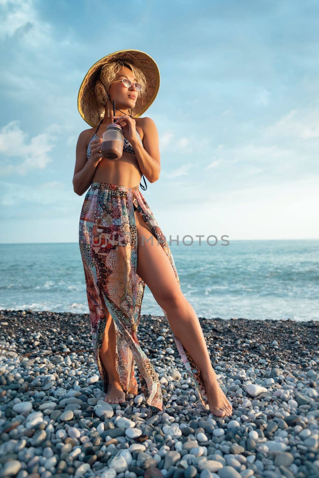 beautiful girl with a smoothie by the sea in straw Asian triangular hat
