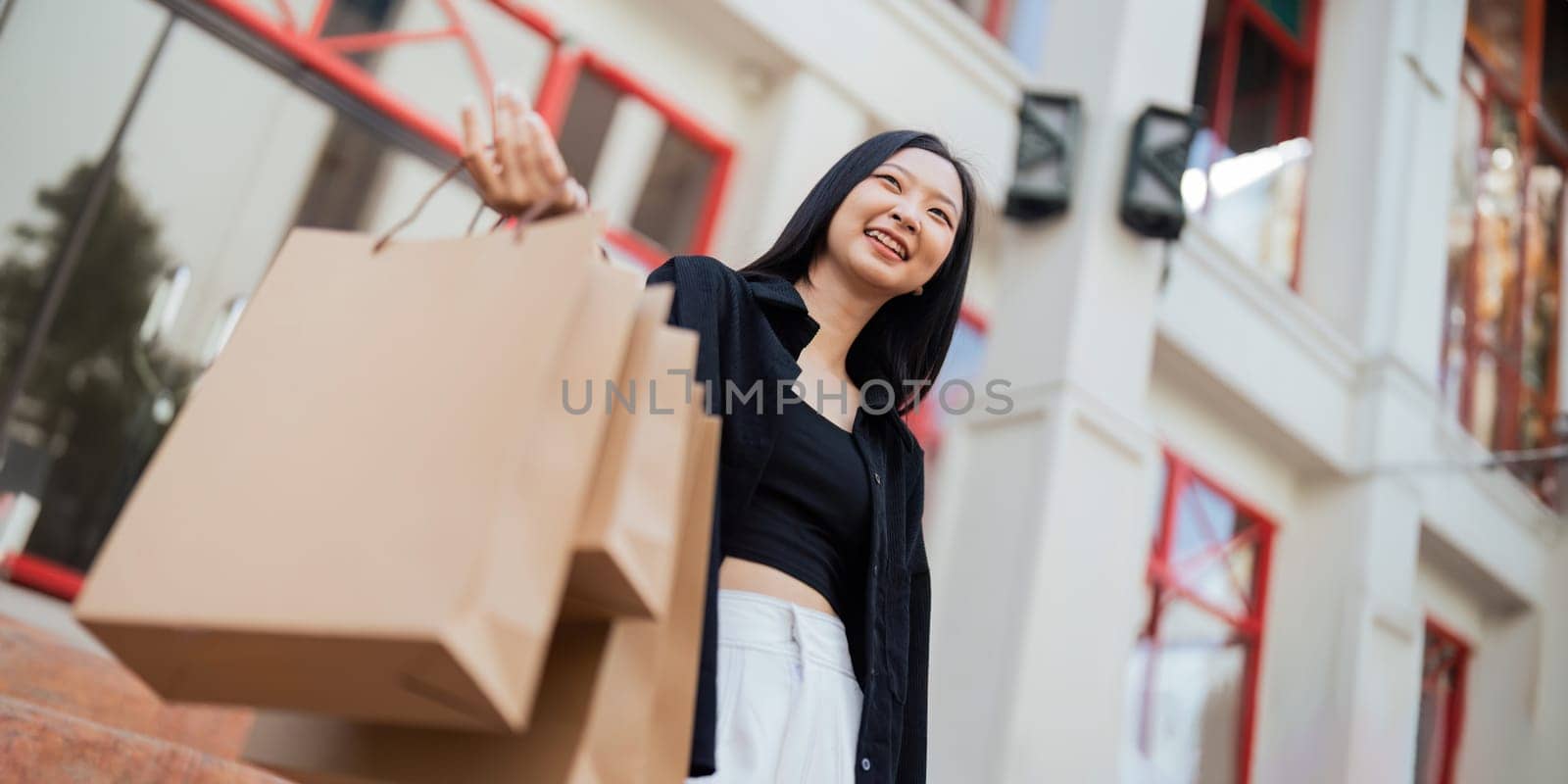 Happy beautiful young stylish woman with shopping bag while walking come out of mall on holiday Black Friday.