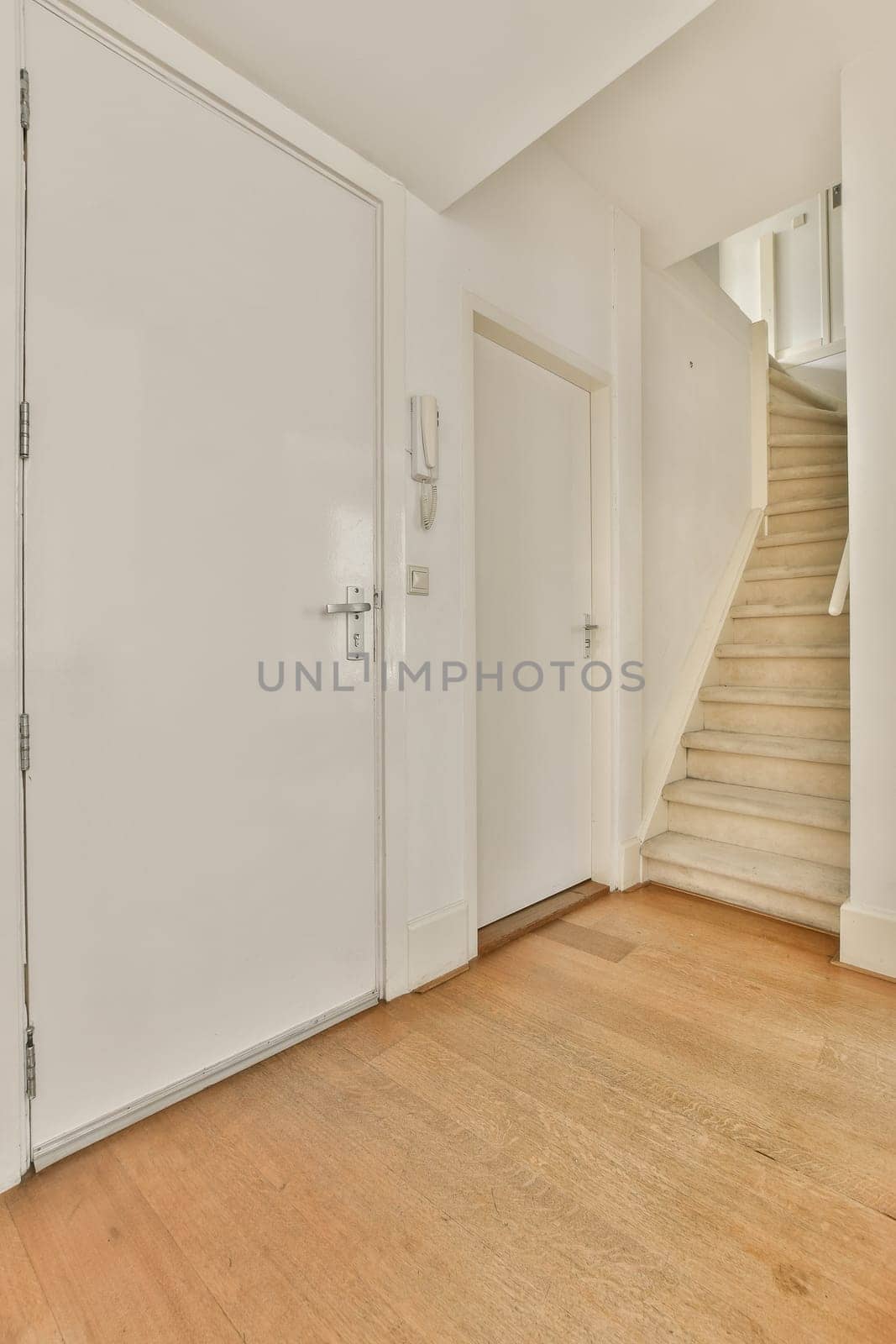 an empty room with white walls and wood flooring on the right side, there is a staircase leading up to the second floor